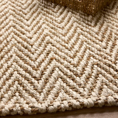 Close-up of a handmade rug featuring a zigzag chevron pattern in beige and tan; a textured object is visible in the top right corner.