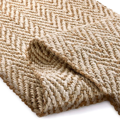 A close-up of a handmade rug in natural jute, displaying its herringbone weave, with one corner partly folded over against a white background.