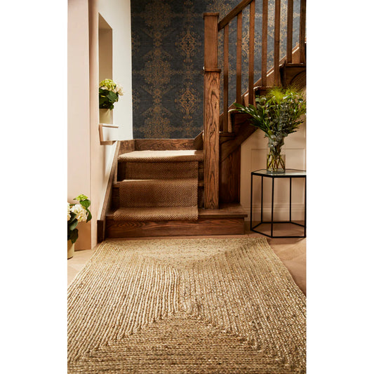 A wooden staircase with a textured runner, an eco-friendly rug on the floor, dark patterned wallpaper, and potted plants arranged on the stairs as well as on a small round table.