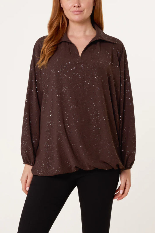 A woman dressed in a vegan-friendly, long-sleeved dark brown blouse with a collar and subtle white speckles, teamed with black trousers—ideal for a festive wardrobe.