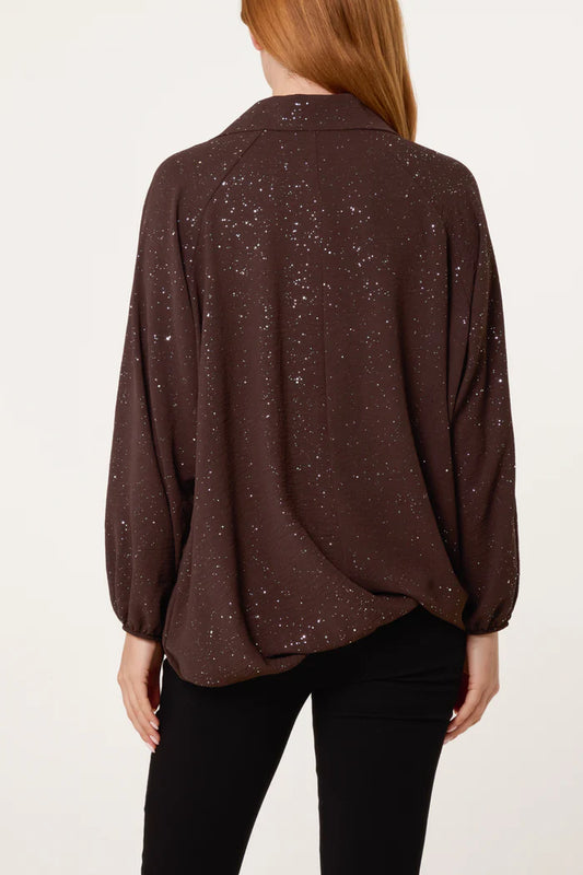 A person wearing a loose-fitting, long-sleeved Metallic Glitter Collar Blouse in dark brown, seen from the back and paired with black trousers—a perfect addition to any festive wardrobe.