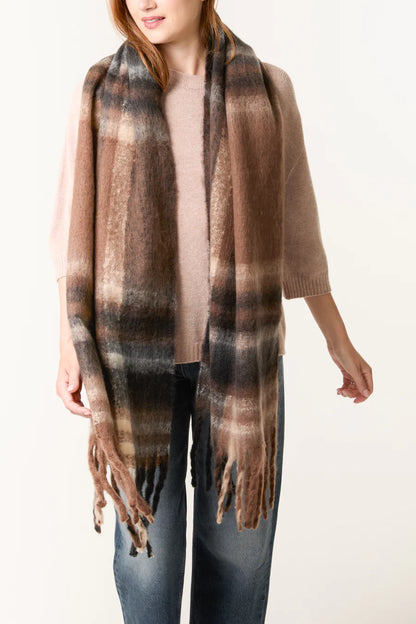 A person wearing a beige jumper and blue jeans, wrapped in a long, checked scarf with fringed ends—a stylish vegan accessory that completes the outfit.