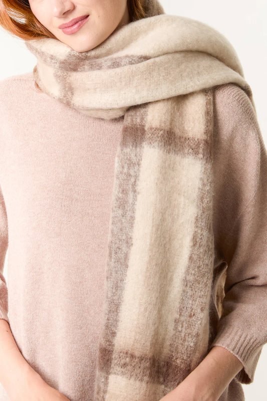 A person wearing a light beige jumper and a large, soft cream checked scarf with tassels wrapped around their neck.