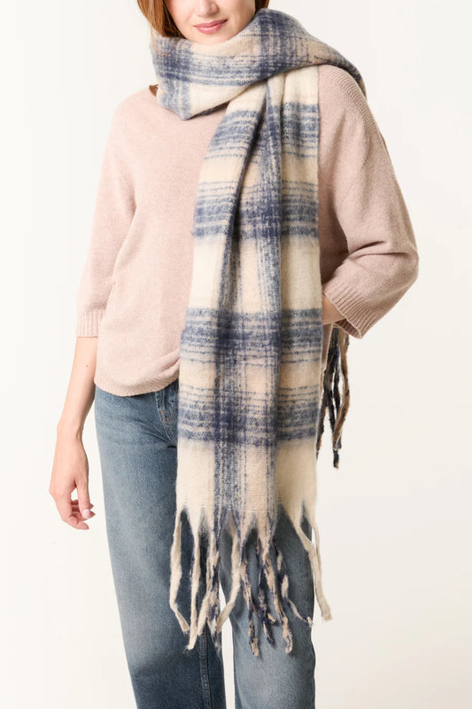 A person wearing a light pink jumper, blue jeans, and a large, vegan-friendly tartan scarf in cream and blue hues.
