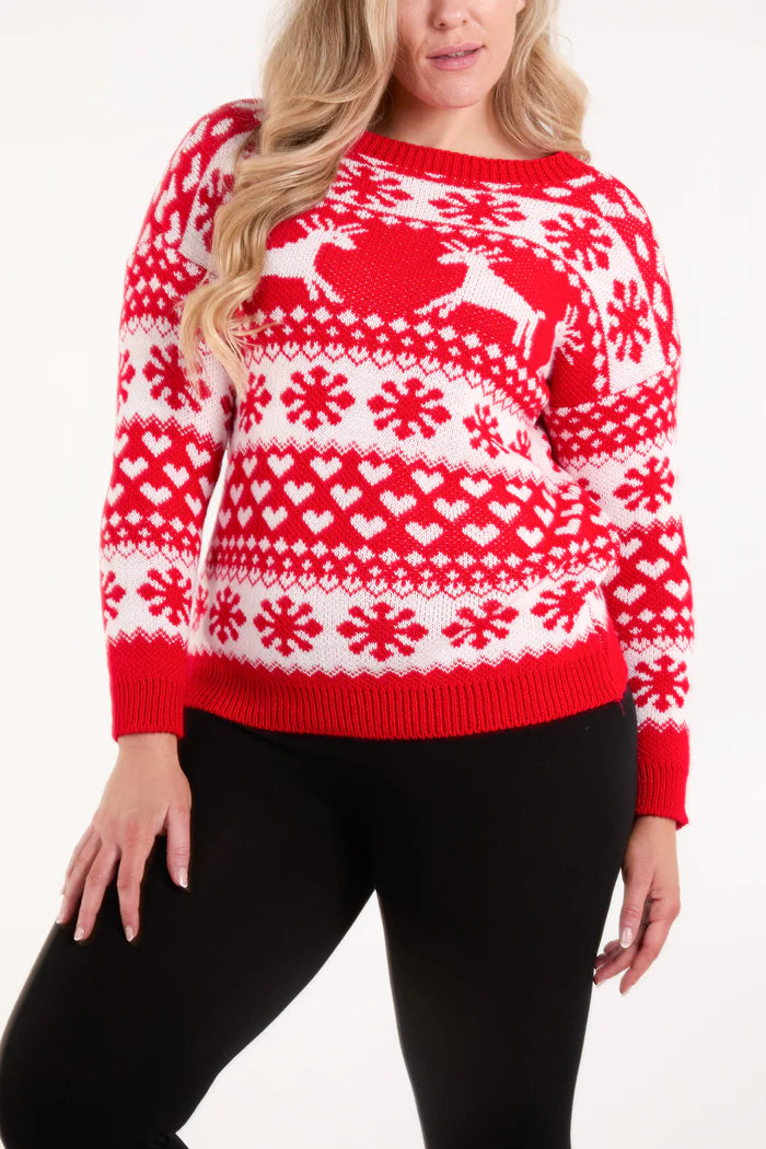 A person wearing a festive jumper with red and white snowflake, heart, and reindeer patterns, paired with black trousers.