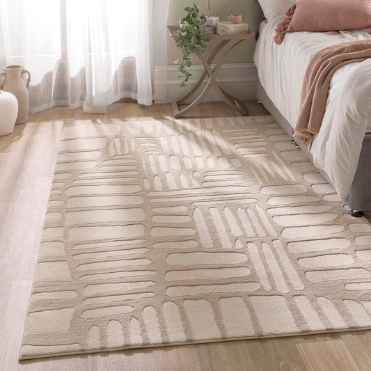A vegan cream rug with a geometric pattern rests on a wooden floor beside a bed, accompanied by a side table, decorative items, and sunlight streaming through sheer curtains.