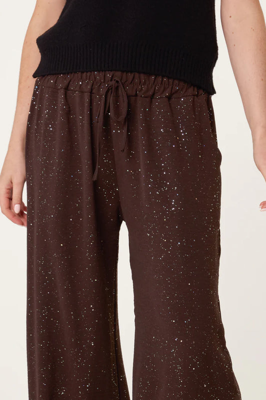 A person wears brown, wide-leg trousers with a drawstring waist and subtle metallic glitter details, paired with a black top.
