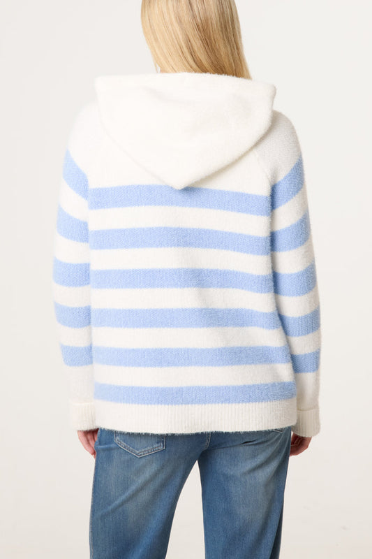 A person with long blonde hair, dressed in a cosy striped hoodie in white and light blue and blue jeans, seen from behind.
