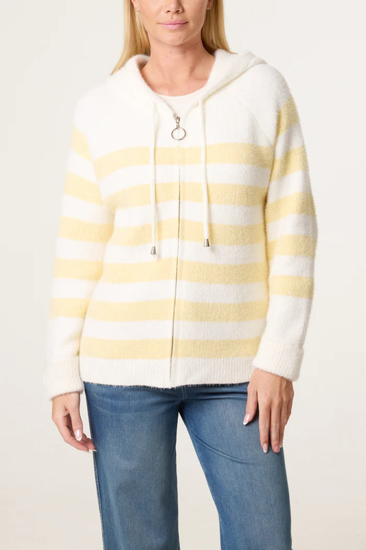 A person wearing a zip-up cosy striped hoodie with white and pale yellow stripes and blue jeans, standing against a plain background.
