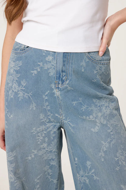 Person wearing wide-leg floral print jeans made from vegan denim and a white top, featuring a vintage-inspired silhouette with one hand on their hip.
