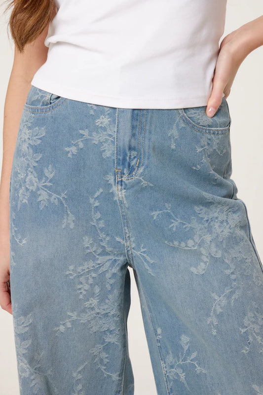 Person wearing wide-leg floral print jeans made from vegan denim and a white top, featuring a vintage-inspired silhouette with one hand on their hip.