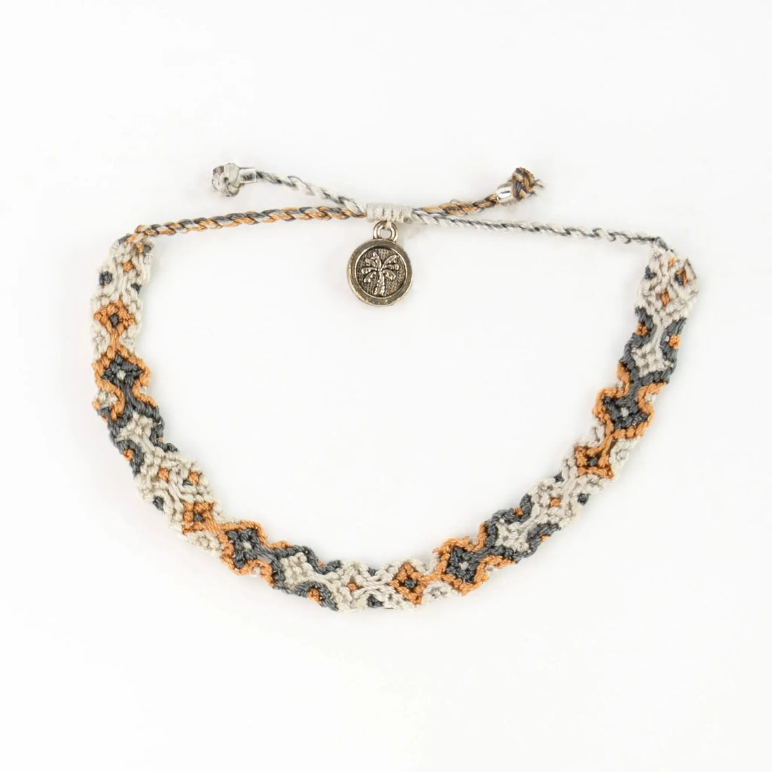 A handwoven Bali bracelet in cream, grey, and orange with a small round metal charm attached, shown on a white background. Supplied in eco-friendly packaging.
