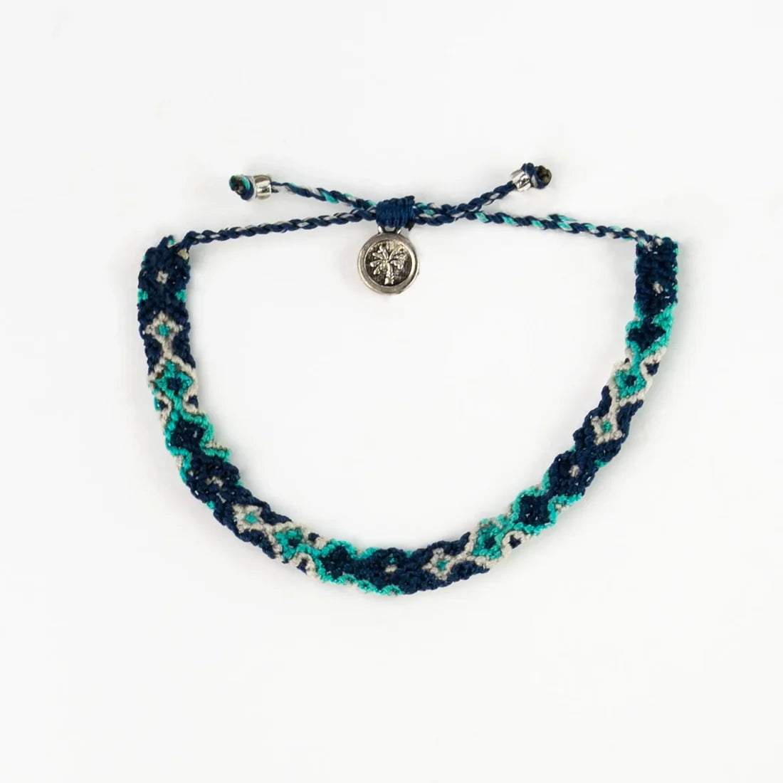A blue, teal, and white handwoven macramé bracelet with adjustable knots and a small round metallic charm at the centre—explore the sustainable jewellery style of a Leme Surf Bracelet.