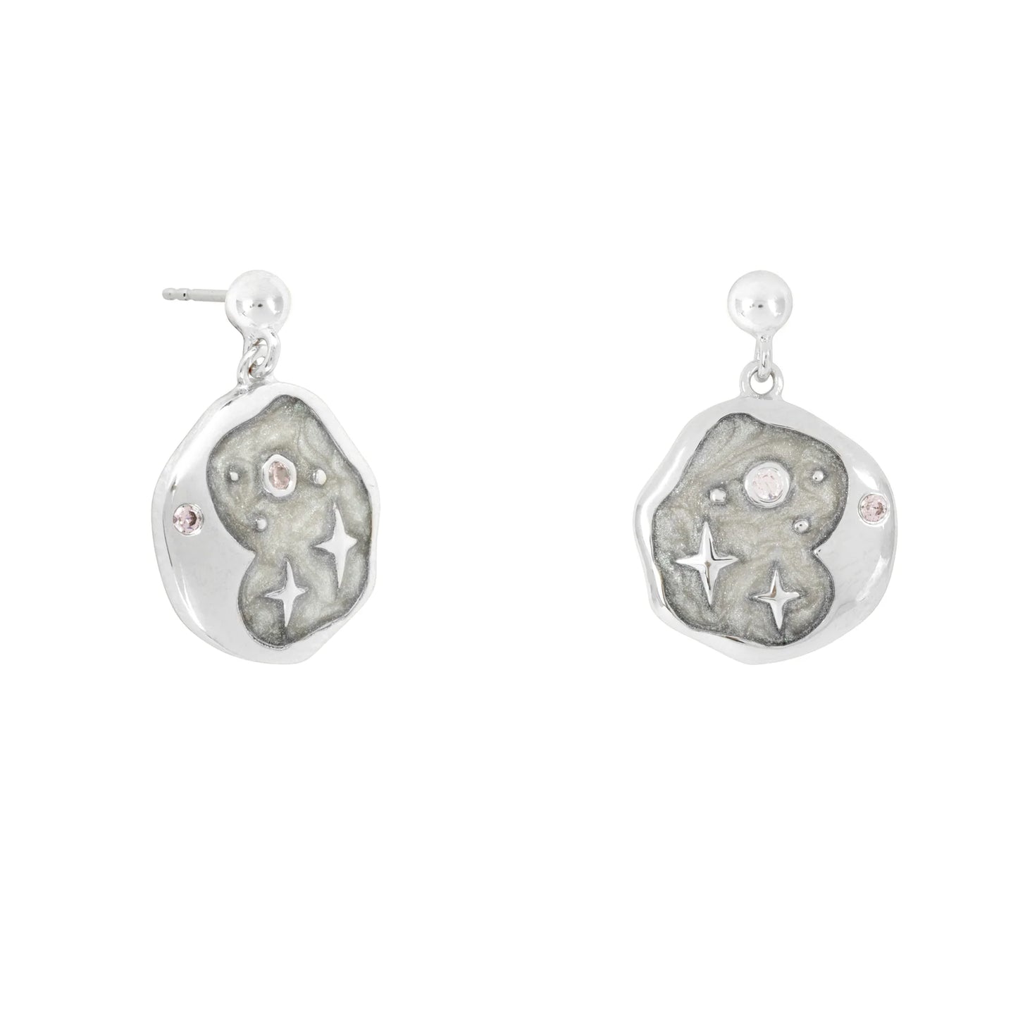 Pair of celestial earrings crafted from hypoallergenic silver, with irregular round shapes adorned with star and jewel-like motifs, displayed against a textured grey background.