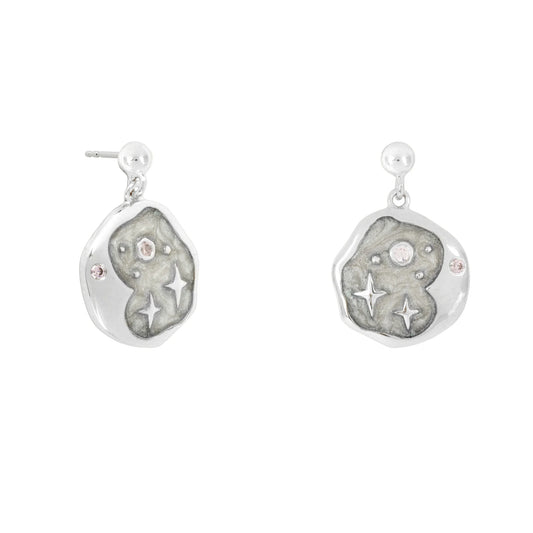 Pair of celestial earrings crafted from hypoallergenic silver, with irregular round shapes adorned with star and jewel-like motifs, displayed against a textured grey background.