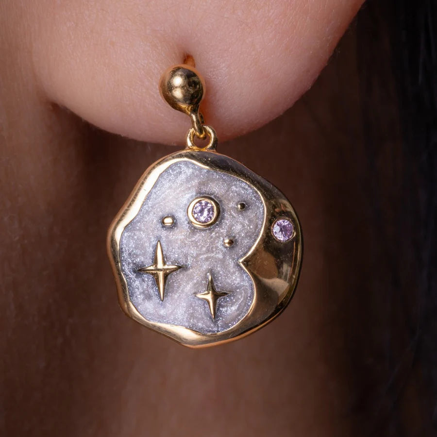 A gold and silver earring with star and dot motifs, adorned with two small gemstones, captures the allure of celestial jewellery as it gleams on a person's ear.