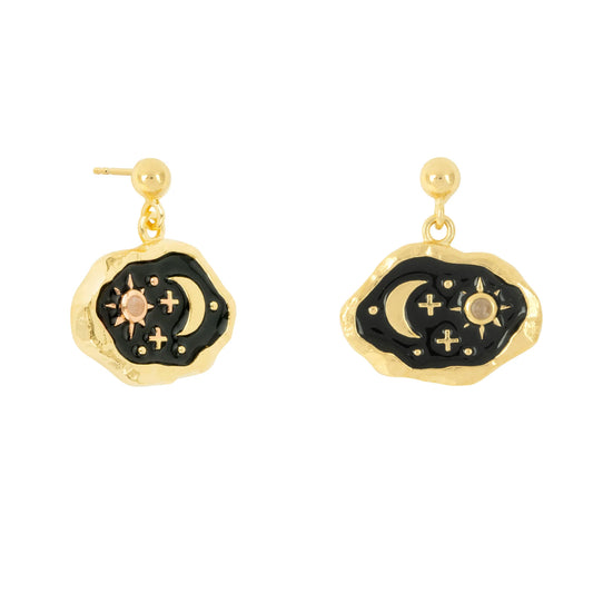 Gold drop earrings with irregular-shaped midnight black enamel centres, adorned with crescent moon, star, and cross designs in gold and silver tones.