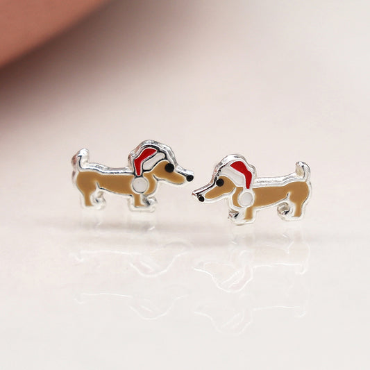 A pair of dachshund-shaped stud festive earrings with red and white Father Christmas hats, displayed on a light-coloured surface.