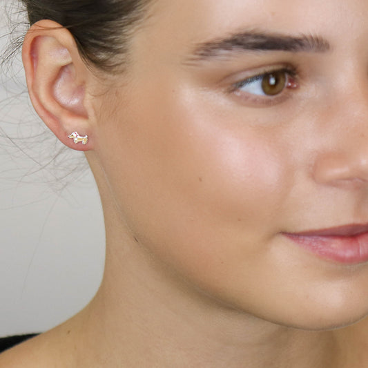 A close-up of a person’s face displaying festive holiday earrings—a small dog-shaped stud worn on their left ear.