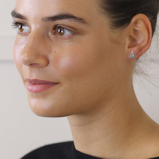 A woman with clear skin and dark hair wears festive earrings—a small, triangular stud—paired with a black top. She looks slightly to the side and smiles softly.