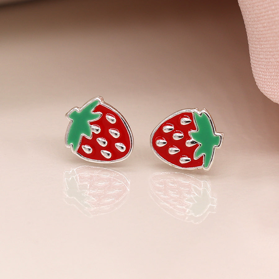 A pair of luxurious strawberry-shaped stud earrings crafted in sterling silver, adorned with vibrant red and green enamel, elegantly rest on a reflective surface.