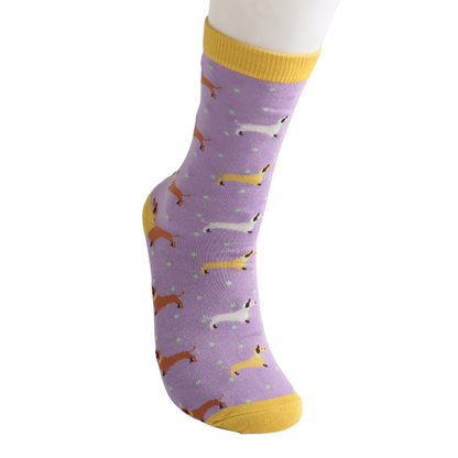 A lavender bamboo sock with a yellow toe and cuff, featuring a playful dachshund pattern in various colours and small green spots.