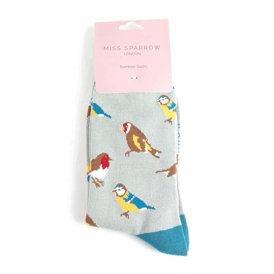 A pair of light grey Garden Birds Socks featuring colourful bird illustrations, packaged with a pink label reading Miss Sparrow London vegan-friendly bamboo blend socks.