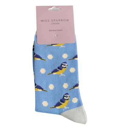 A pair of vegan-friendly cornflower socks featuring yellow and blue bird and white polka dot patterns, labelled Miss Sparrow London Bamboo Socks on a pink tag.
