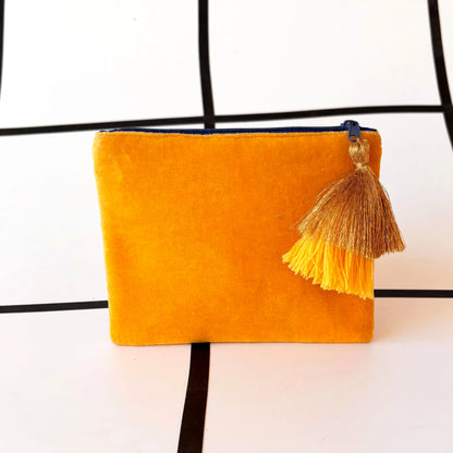 A yellow velvet pouch with a gold and yellow tassel, adorned with delicate glass bead detailing, resting on a white surface with a black grid pattern.