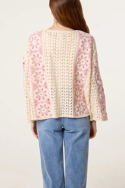 Individual dressed in a cream and pink floral crochet cardigan with vintage appeal and light blue jeans, viewed from behind against a plain light-coloured background.