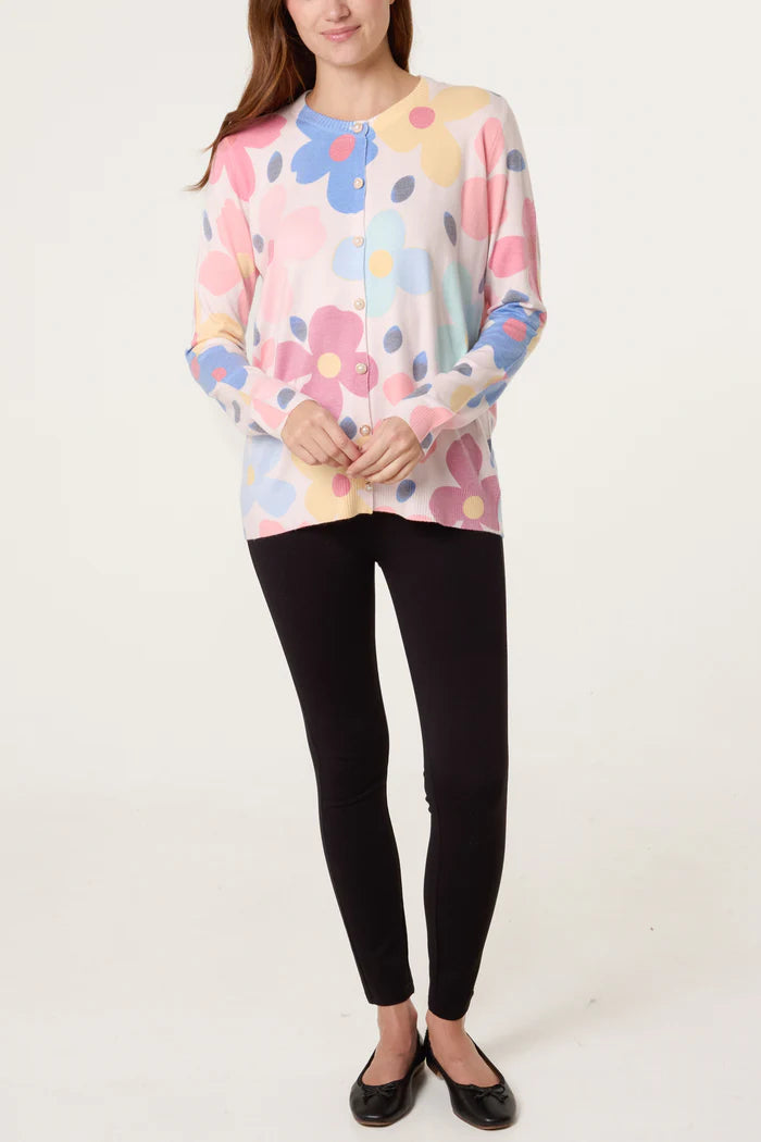 A person wearing a pastel floral cardigan with pearl buttons, black leggings, and black ballet pumps stands against a plain white background.