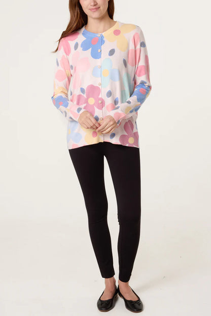 A person wearing a pastel floral cardigan with pearl buttons, black leggings, and black ballet pumps stands against a plain white background.