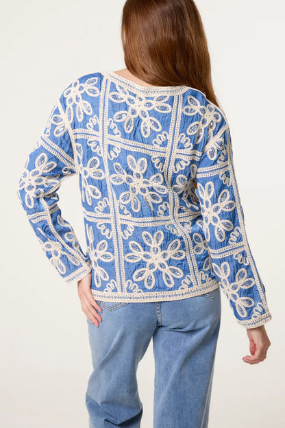 A person with long brown hair, dressed in a blue Sequin Flower Cardigan and blue jeans, seen from the back.