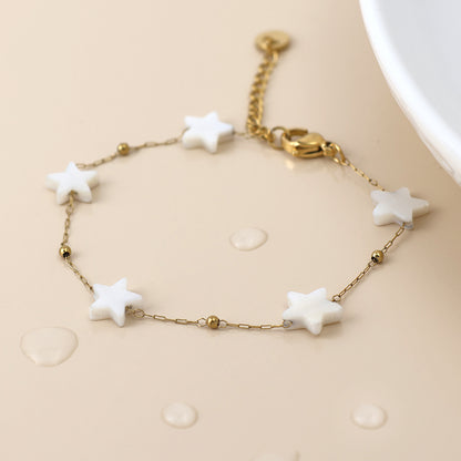Gold star bracelet with five white star-shaped beads and gold accents, shown on a light surface with water droplets—a delicate piece of celestial jewellery.
