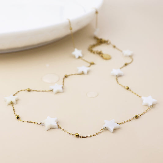 Tarnish-resistant gold chain necklace featuring white star-shaped beads and small gold beads, displayed on a light beige surface beside a white dish.