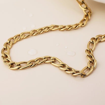 A close-up of a tarnish-resistant, waterproof gold-plated necklace featuring irregular links, resting on a light surface with several water droplets nearby.