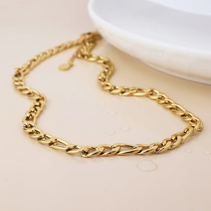 A stylish, tarnish-resistant gold chain necklace with a twisted link design lies on a light surface beside a white dish, water droplets accentuating its waterproof gold-plated gleam.