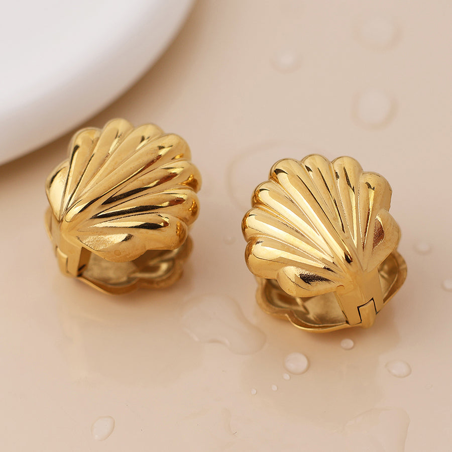 Pair of gold, clamshell earrings on a beige surface with water droplets—stylish seaside jewellery ideal for beach adventures.
