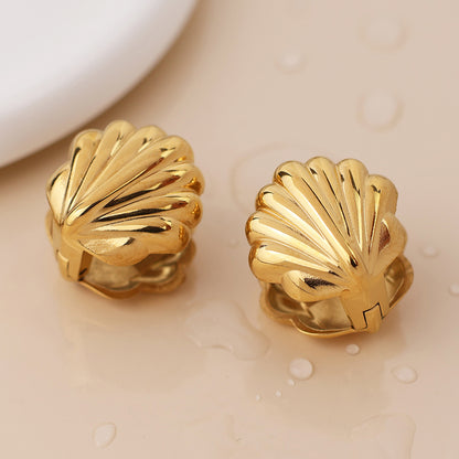 Pair of gold, clamshell earrings on a beige surface with water droplets—stylish seaside jewellery ideal for beach adventures.