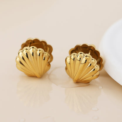 A pair of seaside-chic, gold clam shell earrings displayed on a light-coloured surface.