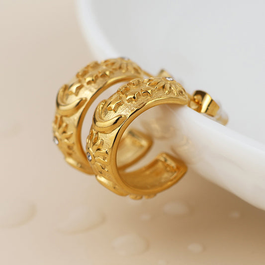 A pair of gold-plated earrings with intricate floral patterns rests on the edge of a white ceramic dish.