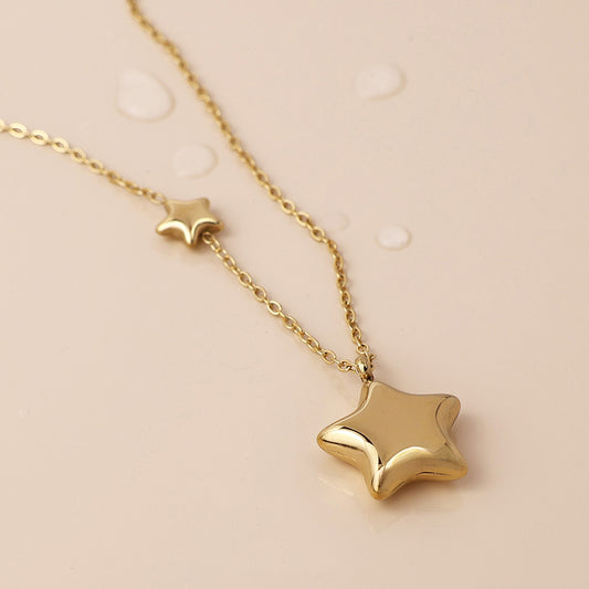 Double star necklace with two star-shaped pendants lies on a light beige surface scattered with water droplets—a striking piece of celestial jewellery.