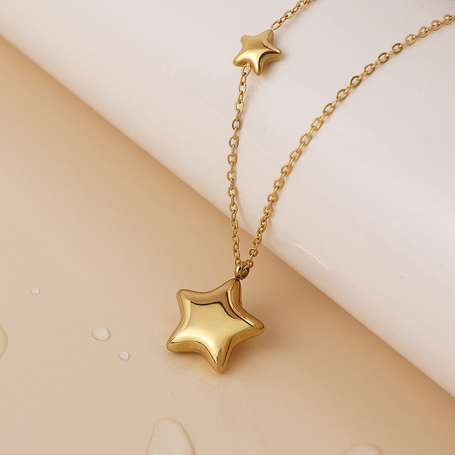 Celestial jewellery at its finest—a waterproof gold double star necklace, featuring two star-shaped pendants resting on a light beige surface adorned with water droplets.