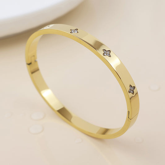 A gold-plated crystal bangle adorned with star-shaped accents and tiny embedded crystals, shown on a light surface, brings an elegant touch with its waterproof finish.
