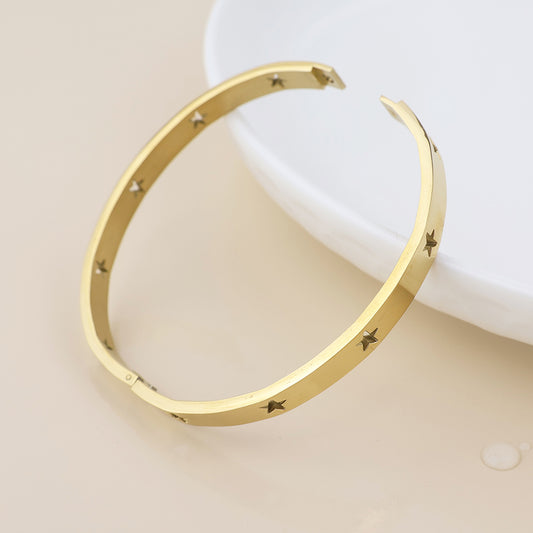 A celestial jewellery piece, this waterproof gold-plated bangle featuring small star-shaped cut-outs is shown beside a white ceramic dish on a light beige surface.