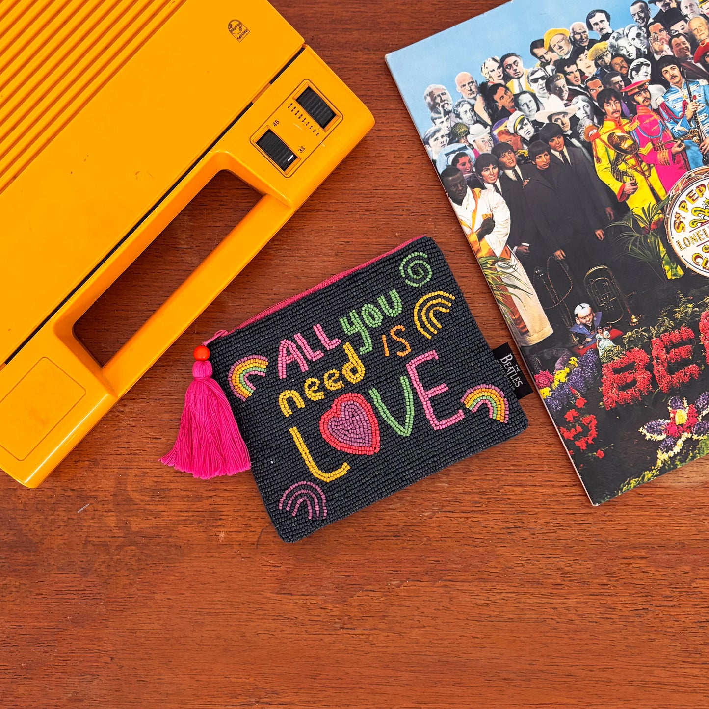 A yellow portable record player, a Beatles Sgt. Pepper’s vinyl, and an All You Need Is Love pouch—ideal Beatles accessories—rest on a wooden surface.