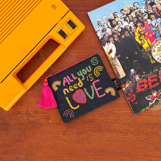 A yellow portable record player, a Beatles Sgt. Pepper’s vinyl, and an All You Need Is Love pouch—ideal Beatles accessories—rest on a wooden surface.