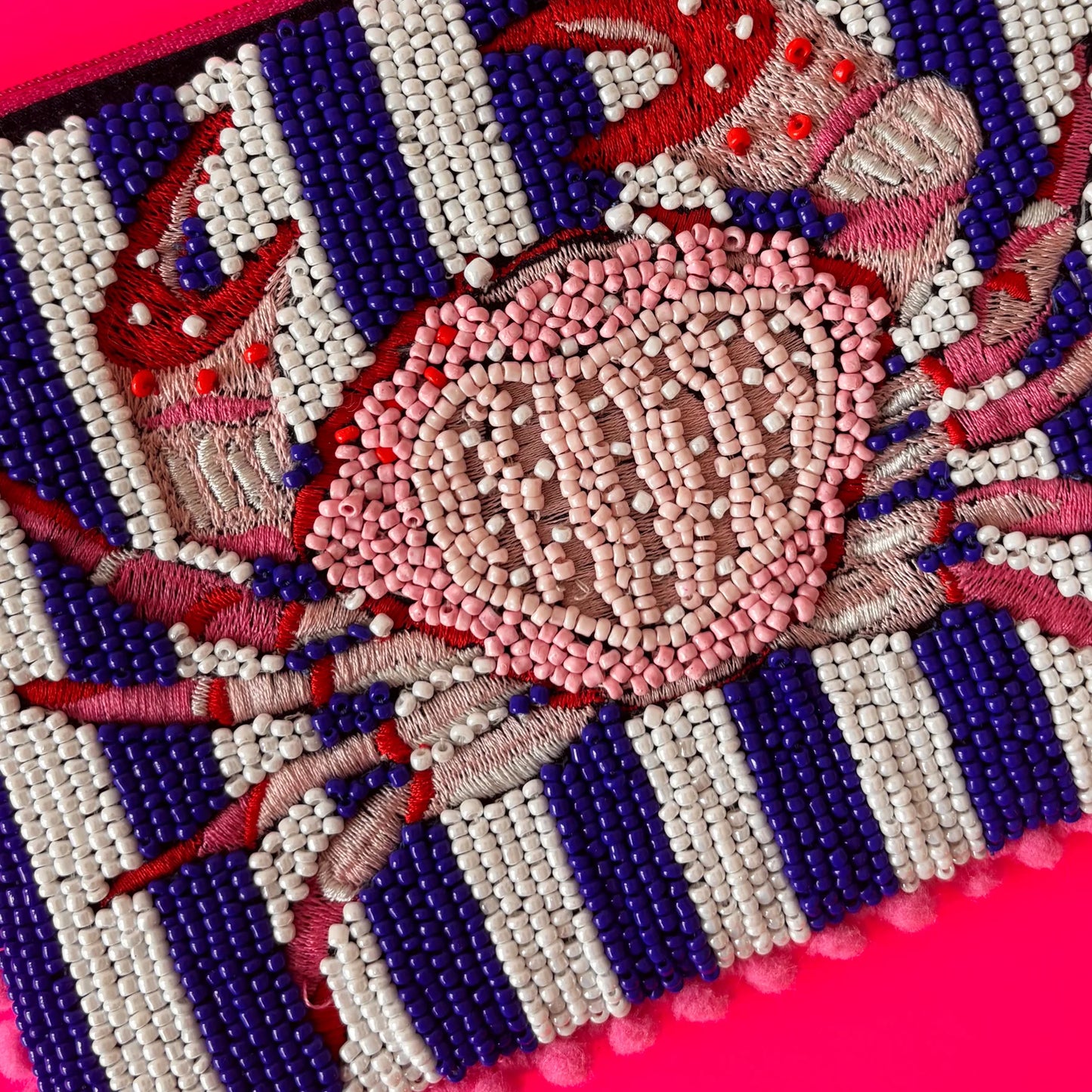 Beaded and embroidered crab motif crafted with red, pink, and white beads on a nautical striped background, set against a vibrant pink surface—ideal for a chic handcrafted pouch.