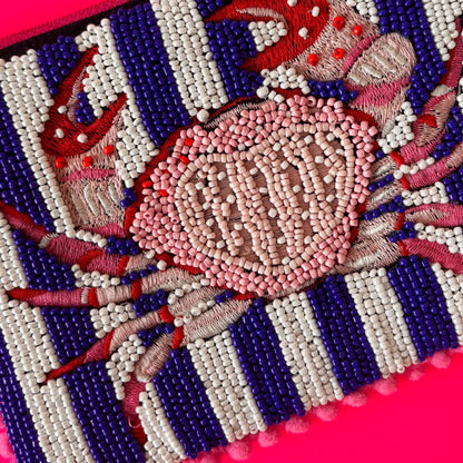 Beaded and embroidered crab motif crafted with red, pink, and white beads on a nautical striped background, set against a vibrant pink surface—ideal for a chic handcrafted pouch.