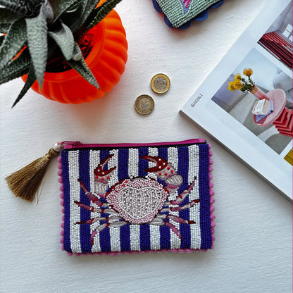 A beaded pouch with blue and white nautical stripes rests next to an orange plant pot, two coins, and an open magazine atop a white surface.